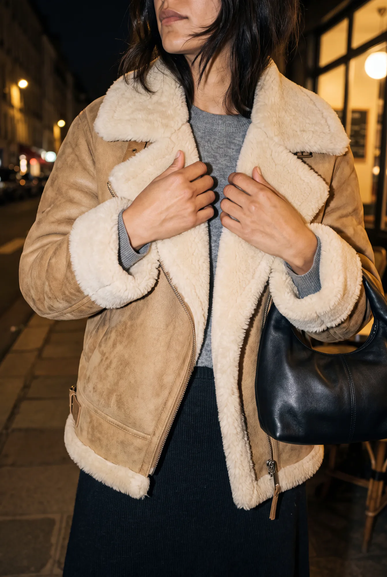A close-up of a woman's torso wearing a tan shearling aviator jacket with cream fleece collar and cuffs, hands at her | The Weight of Winter, Relover